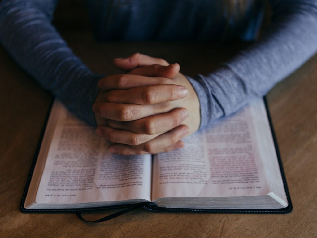 Praying hands over a bible | Share the Gift The Message God's Gift to Us
